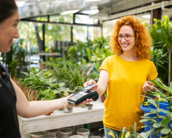 Smiling woman in an orange shirt making a contactless payment at a plant nursery.