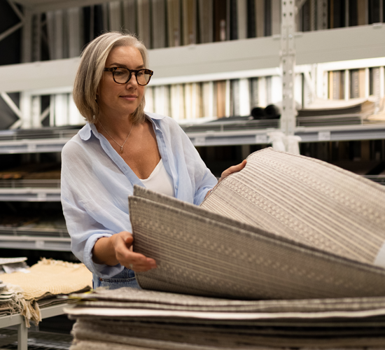 Middle aged woman shopping through a pile of rugs at a flooring store. 