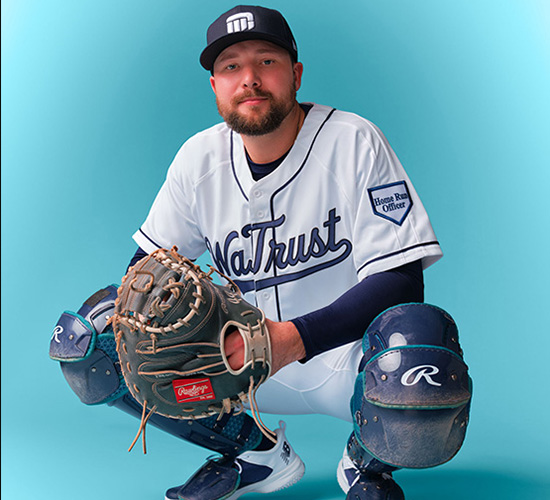 Cal Raleigh wearing a Washington Trust Bank jersey and catcher's gear against a teal background.