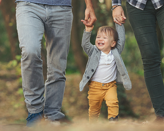 Small child holding hand with parents who are out of frame.